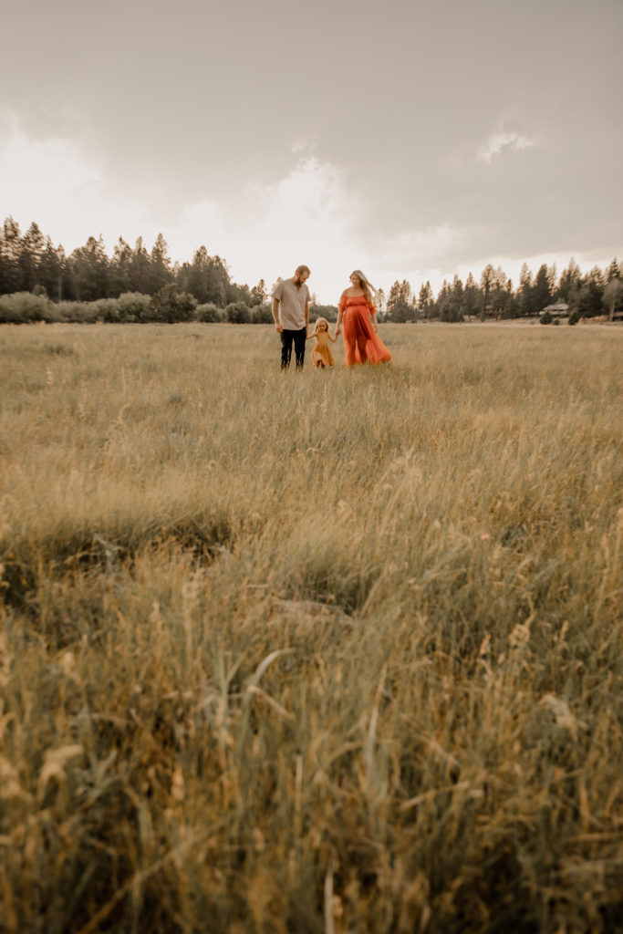 maternity photography session at indian meadows in sisters oregon, family of three walking together in a field